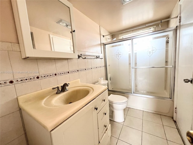 full bathroom featuring tile walls, toilet, vanity, tile flooring, and bath / shower combo with glass door