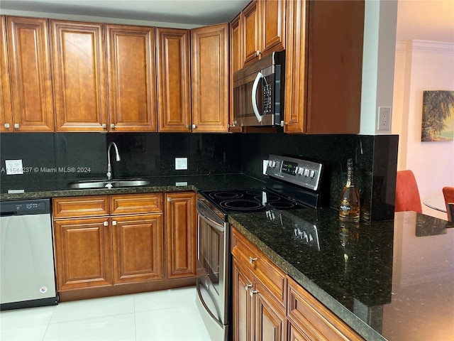 kitchen with dark stone counters, stainless steel appliances, sink, light tile patterned floors, and backsplash