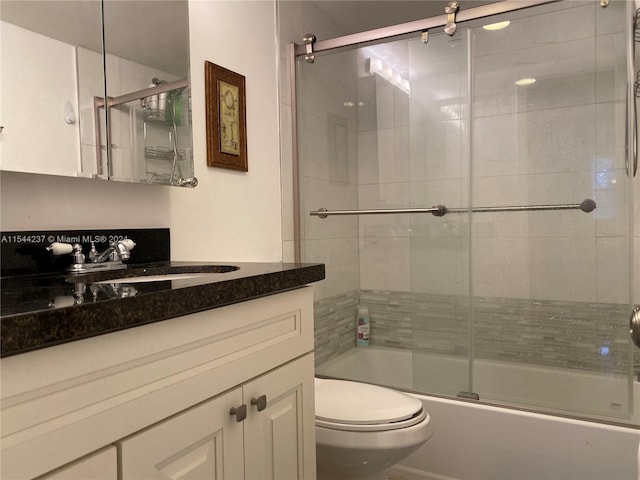 full bathroom with combined bath / shower with glass door, toilet, and vanity