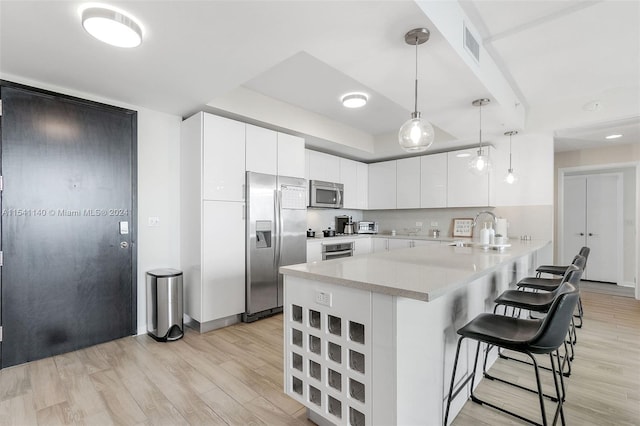 kitchen with appliances with stainless steel finishes, white cabinetry, light hardwood / wood-style flooring, and pendant lighting