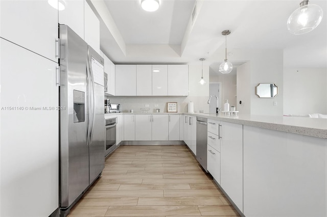 kitchen with hanging light fixtures, appliances with stainless steel finishes, light hardwood / wood-style floors, light stone countertops, and white cabinetry