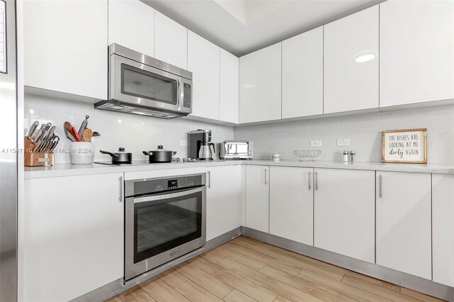 kitchen with tasteful backsplash, light hardwood / wood-style floors, white cabinets, and appliances with stainless steel finishes