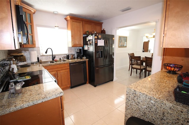 kitchen with pendant lighting, black appliances, sink, decorative backsplash, and light stone counters