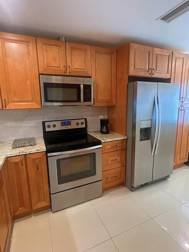 kitchen featuring tasteful backsplash, light stone countertops, light tile patterned floors, and appliances with stainless steel finishes