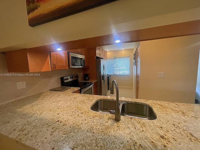 kitchen with kitchen peninsula, light stone counters, sink, and appliances with stainless steel finishes