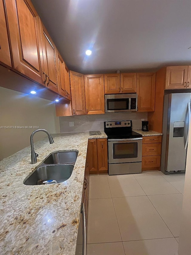 kitchen featuring light stone countertops, sink, light tile patterned floors, and stainless steel appliances