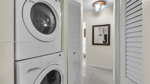 laundry area with light tile patterned flooring, stacked washing maching and dryer, and a textured ceiling