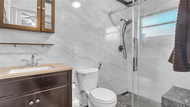 bathroom with vanity, toilet, a shower with shower door, and tile walls