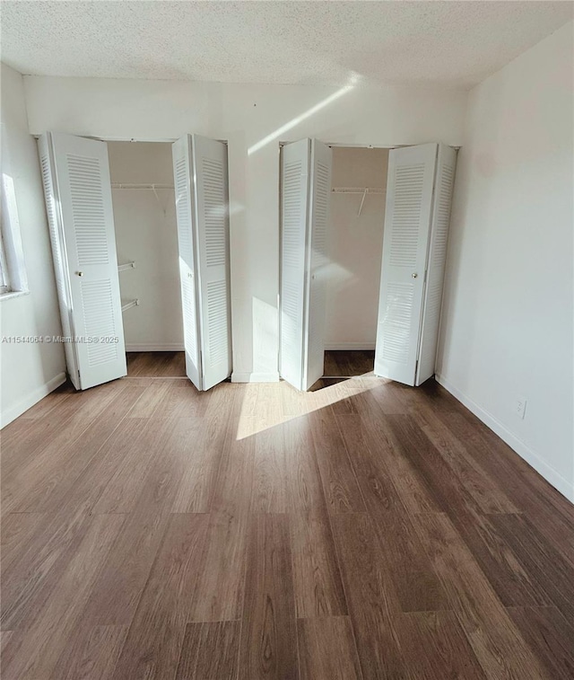 unfurnished bedroom featuring multiple closets, wood-type flooring, and a textured ceiling