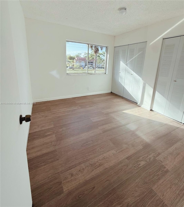 unfurnished bedroom featuring multiple closets, wood-type flooring, and a textured ceiling