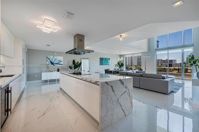 kitchen featuring white cabinetry, light tile flooring, an island with sink, light stone counters, and island exhaust hood