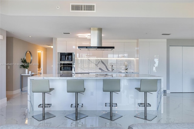 kitchen featuring white cabinets, light stone countertops, a breakfast bar, and island range hood