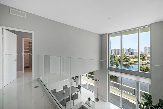 corridor with a water view, a healthy amount of sunlight, and light tile floors