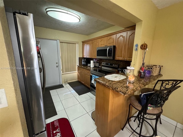 kitchen with light tile patterned flooring, stainless steel appliances, kitchen peninsula, and dark stone countertops