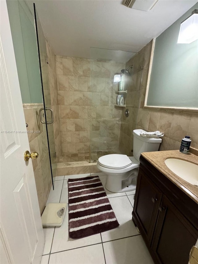 bathroom featuring tile walls, vanity, toilet, a shower with door, and tile patterned floors