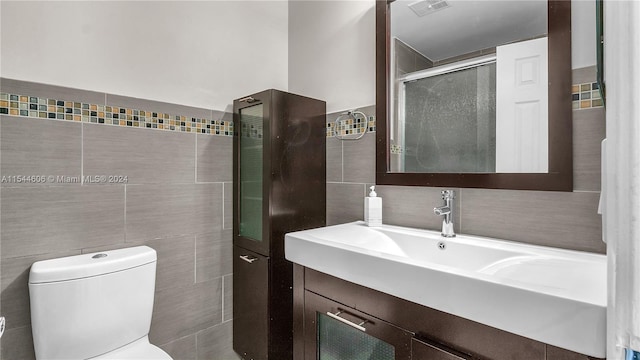 bathroom featuring tile walls, toilet, a shower with door, and vanity