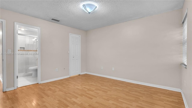 unfurnished bedroom featuring light hardwood / wood-style floors, a textured ceiling, and ensuite bath