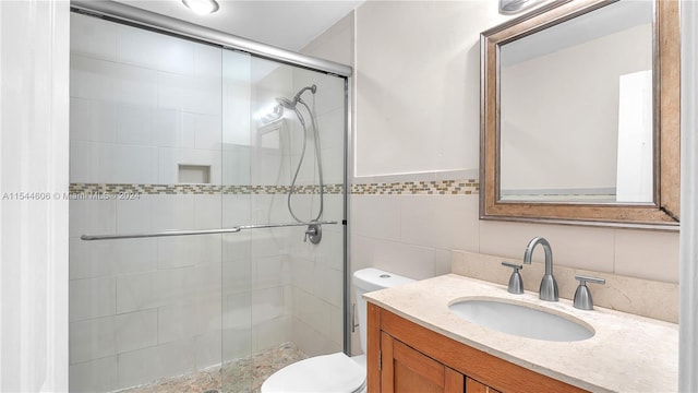 bathroom featuring toilet, a shower with door, vanity, backsplash, and tile walls