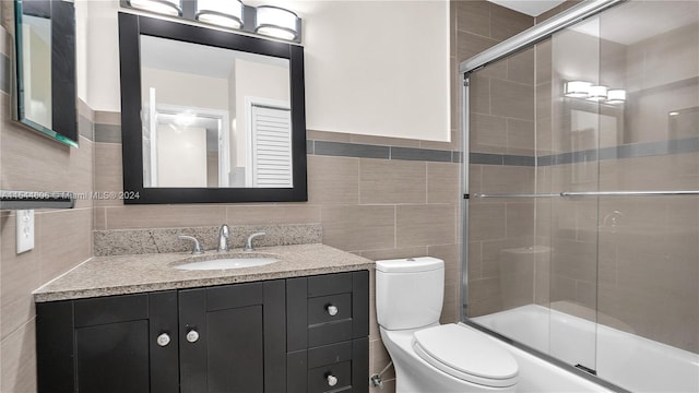 full bathroom featuring toilet, shower / bath combination with glass door, vanity, backsplash, and tile walls