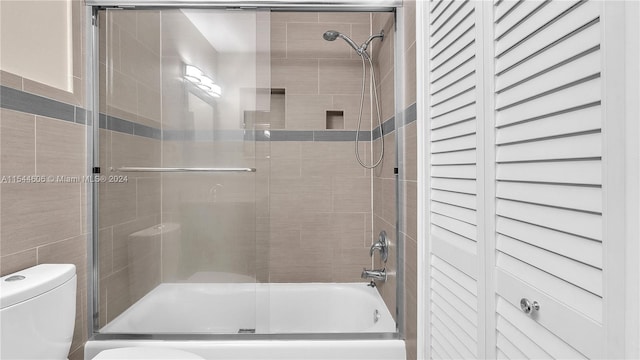 bathroom featuring tile walls, toilet, and bath / shower combo with glass door