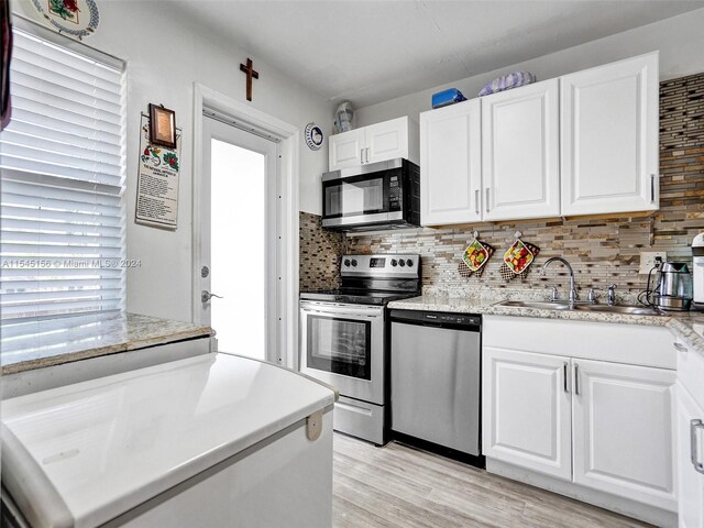 kitchen with sink, backsplash, white cabinetry, stainless steel appliances, and light hardwood / wood-style flooring