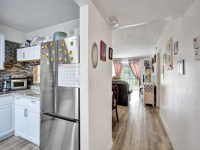 kitchen with tasteful backsplash, a textured ceiling, white cabinetry, stainless steel refrigerator, and light hardwood / wood-style flooring