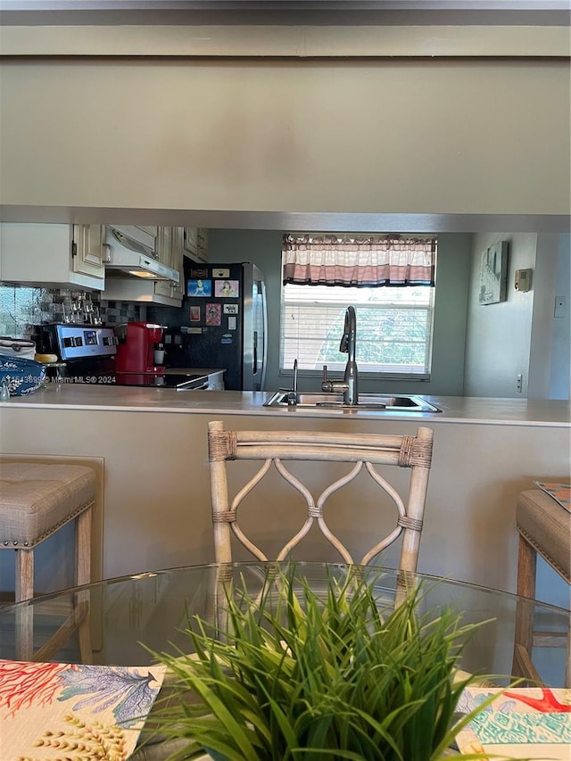 kitchen featuring stainless steel fridge, tasteful backsplash, range, wall chimney exhaust hood, and sink