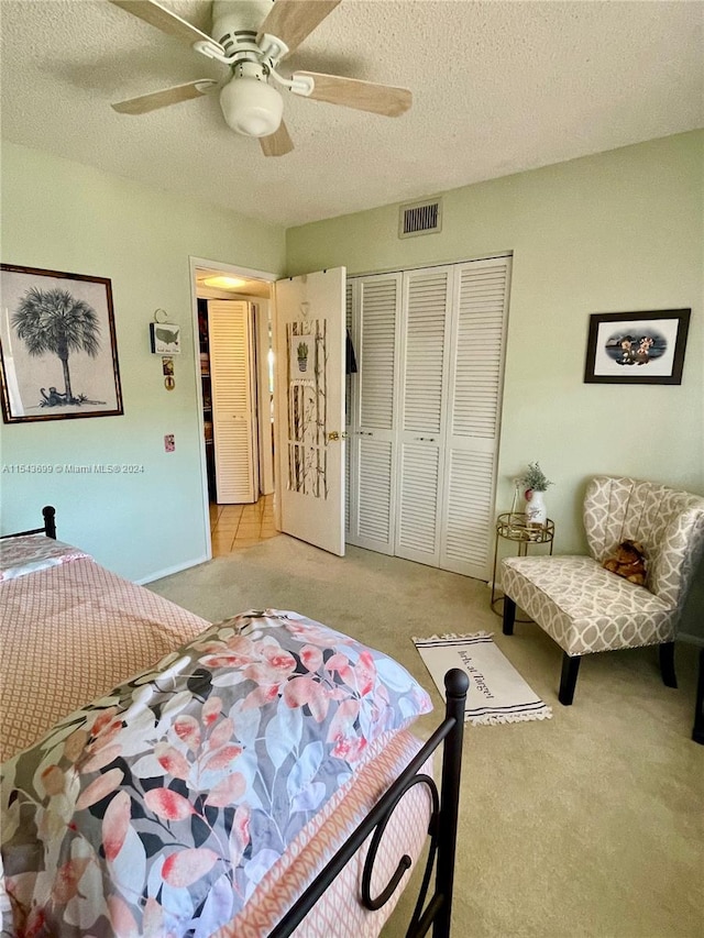 carpeted bedroom with ceiling fan, a closet, and a textured ceiling