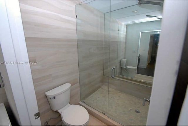 bathroom featuring tile walls, toilet, and a shower with shower door