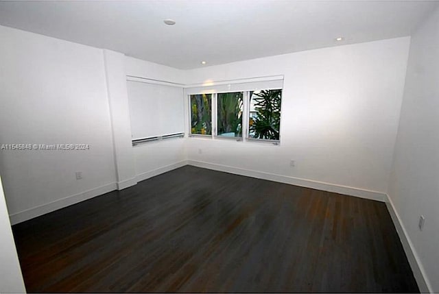 unfurnished room featuring baseboard heating and dark hardwood / wood-style flooring