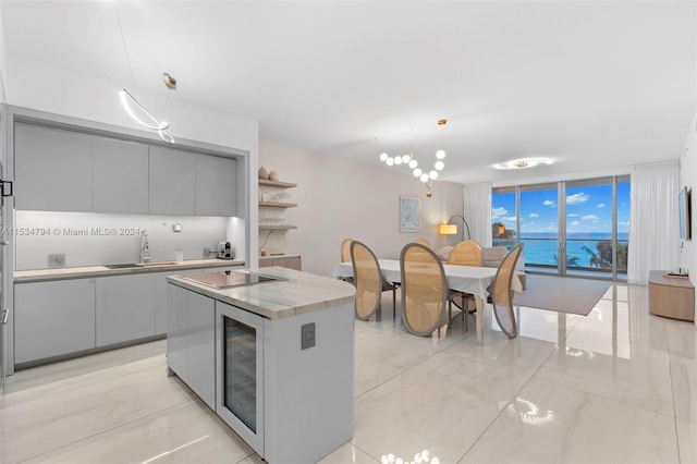 kitchen featuring black electric stovetop, sink, decorative light fixtures, a kitchen island, and beverage cooler