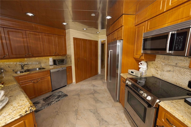 kitchen featuring tasteful backsplash, light stone countertops, appliances with stainless steel finishes, sink, and light tile patterned floors