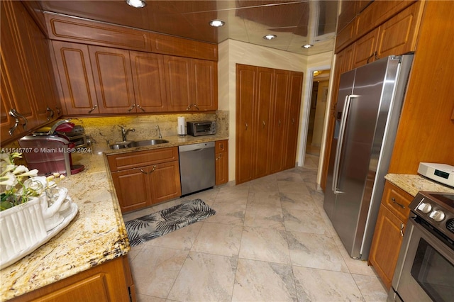 kitchen with sink, appliances with stainless steel finishes, light stone counters, and tasteful backsplash