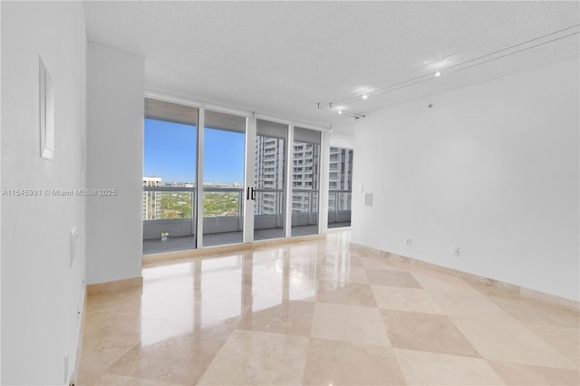 empty room featuring expansive windows, track lighting, and a textured ceiling