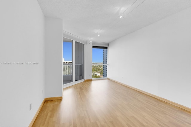 spare room featuring expansive windows, a textured ceiling, and light hardwood / wood-style floors