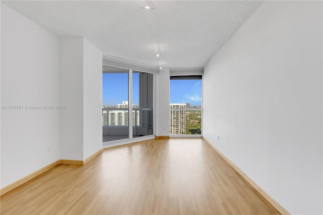 spare room with expansive windows, a textured ceiling, and light wood-type flooring