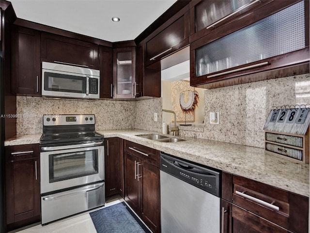 kitchen with light stone countertops, appliances with stainless steel finishes, sink, and decorative backsplash