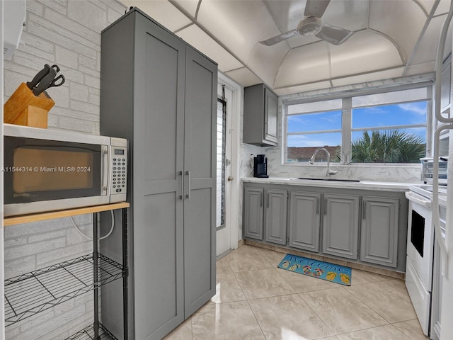 kitchen with gray cabinetry, backsplash, ceiling fan, stainless steel microwave, and sink