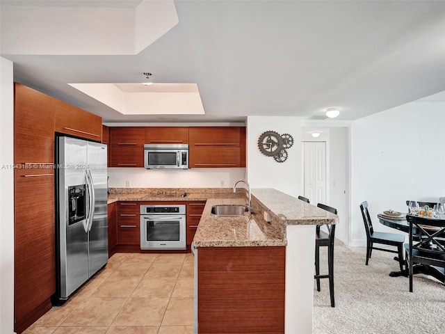 kitchen with light tile floors, light stone countertops, kitchen peninsula, appliances with stainless steel finishes, and sink