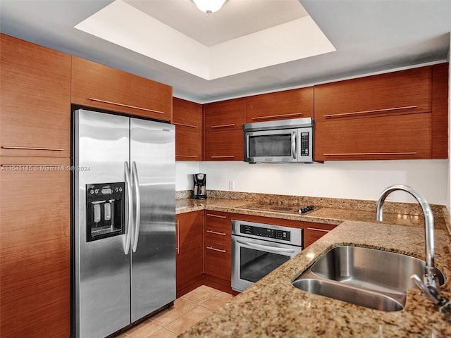 kitchen featuring stainless steel appliances, light tile floors, a tray ceiling, light stone counters, and sink