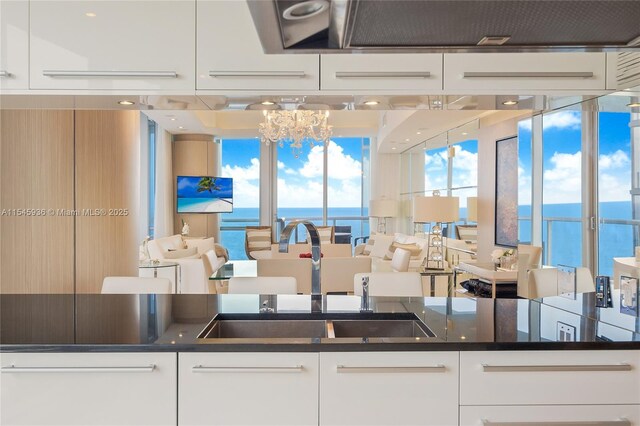 kitchen featuring sink, a water view, white cabinets, and dark stone counters