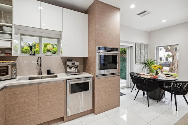 kitchen featuring white cabinetry, stainless steel oven, plenty of natural light, and sink