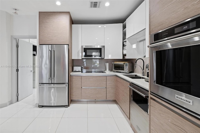 kitchen with light tile patterned floors, sink, appliances with stainless steel finishes, backsplash, and white cabinets