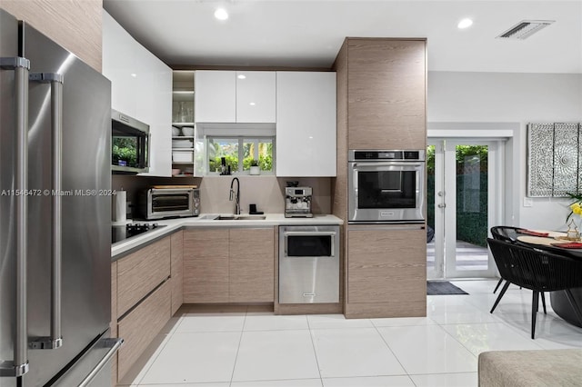 kitchen with white cabinetry, sink, light tile patterned floors, stainless steel appliances, and light brown cabinets