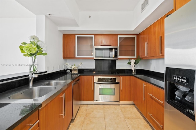 kitchen with appliances with stainless steel finishes, sink, light tile flooring, and dark stone countertops