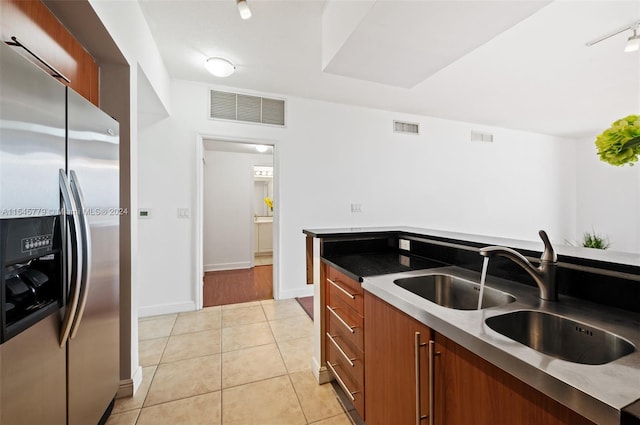 kitchen with sink, light wood-type flooring, dark stone counters, track lighting, and stainless steel refrigerator with ice dispenser