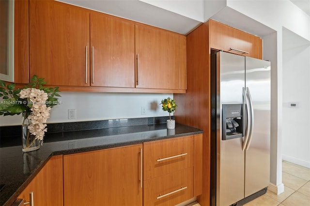 kitchen featuring dark stone countertops, light tile floors, and stainless steel refrigerator with ice dispenser