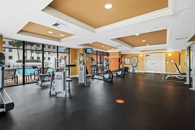 exercise room with a wealth of natural light, a raised ceiling, floor to ceiling windows, and ornamental molding