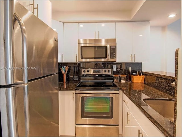 kitchen with stainless steel appliances, white cabinets, sink, and dark stone countertops