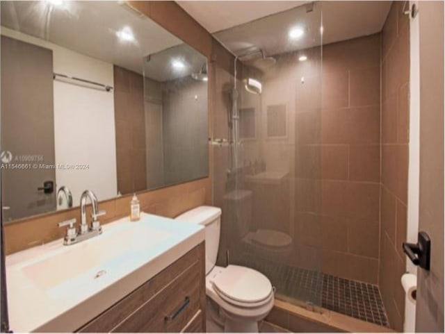 bathroom with vanity with extensive cabinet space, walk in shower, tile walls, and toilet